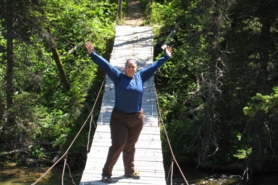 Woman with Lipedema standing with outstretched arms in triumph on a swinging bridge.