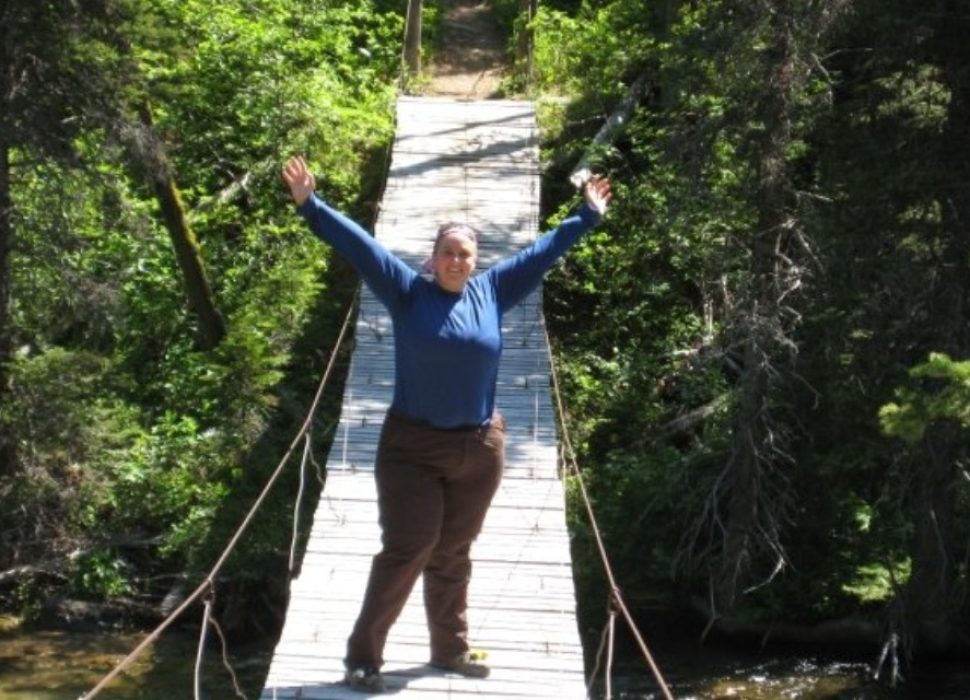 Woman with Lipedema standing with outstretched arms in triumph on a swinging bridge.