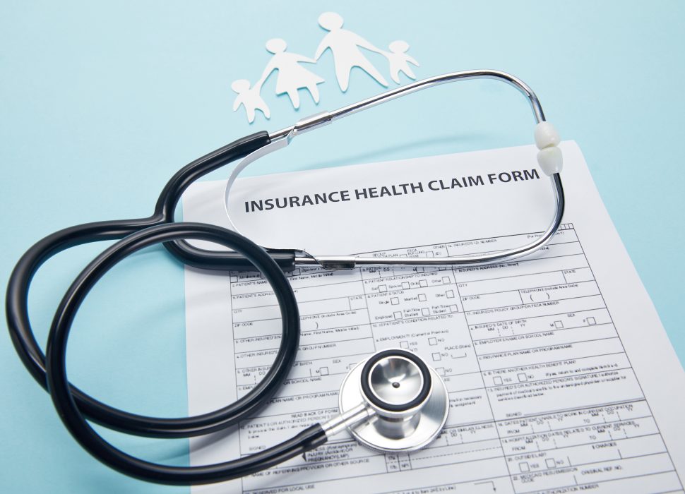 close-up view of insurance health claim form, paper cut family and stethoscope on blue